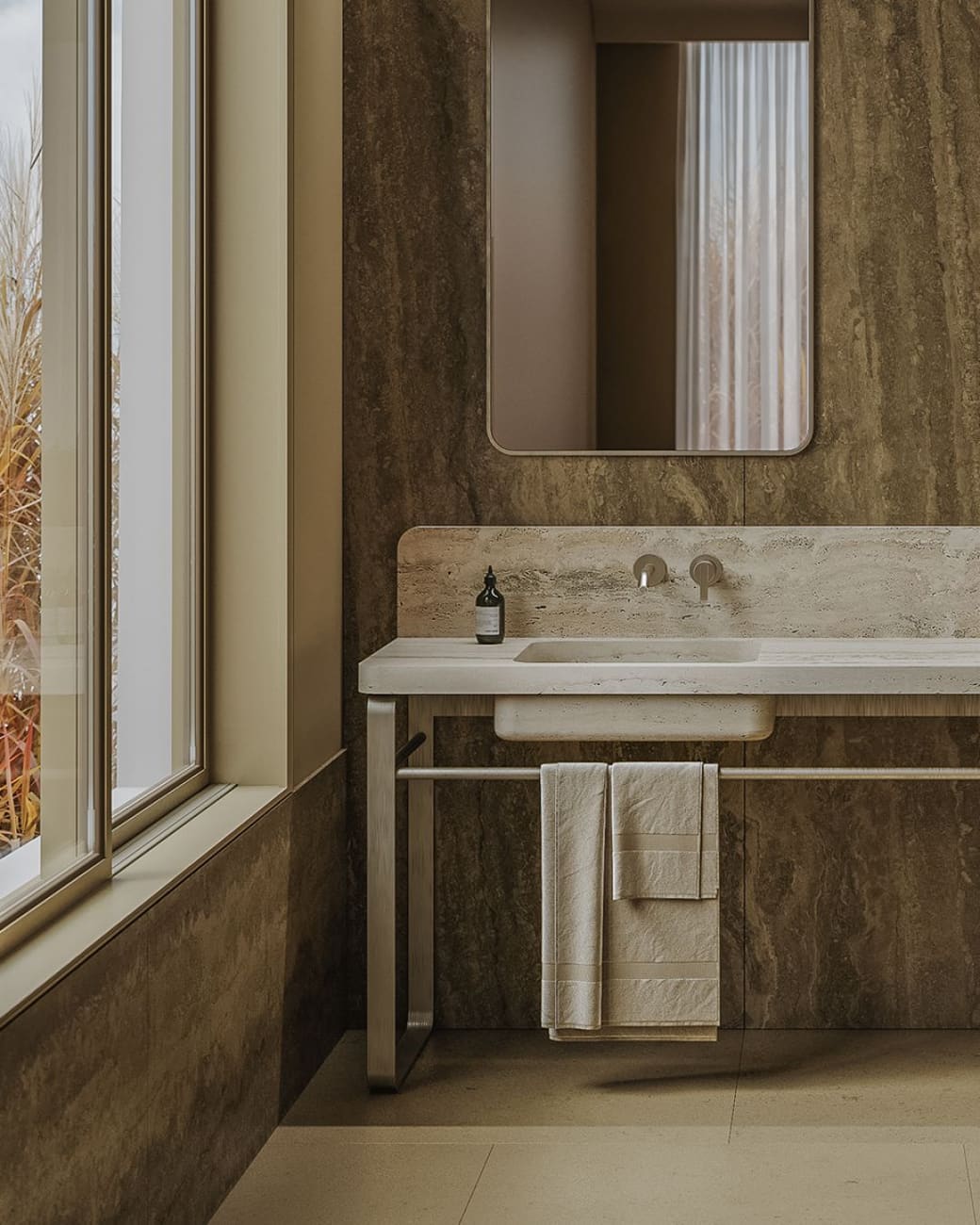 VANUATU travertine washbasin with a splashback, on a metal stand by a window