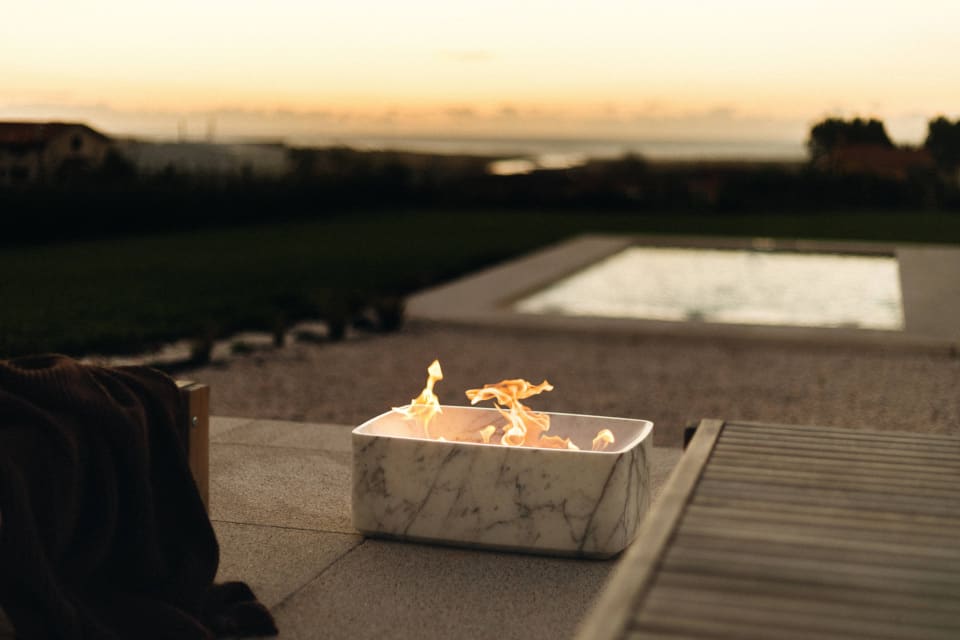 ESSENTIA marble fire pit on a terrace by a swimming pool at dusk